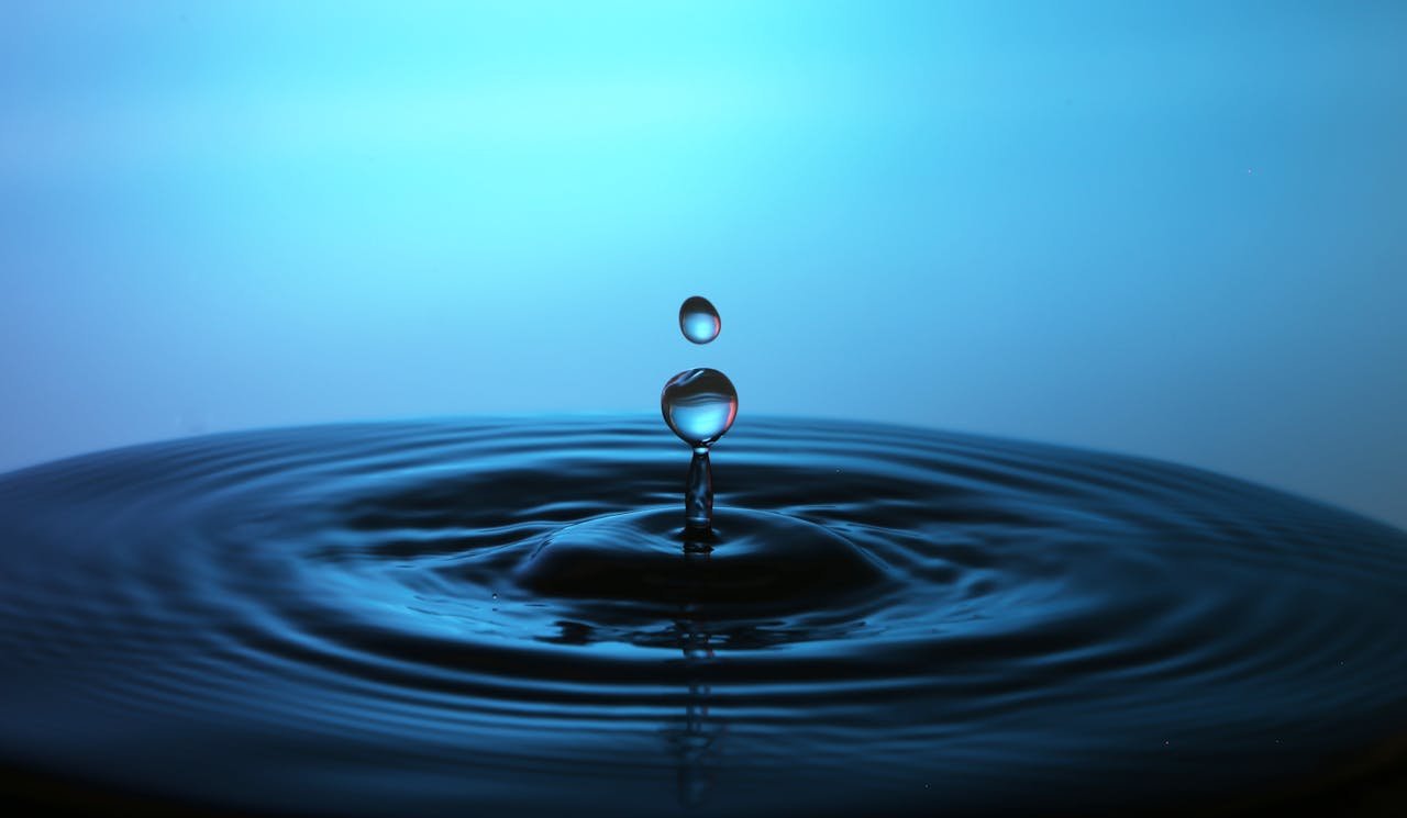 Macro shot of a perfect water droplet splash creating ripples on a blue background.